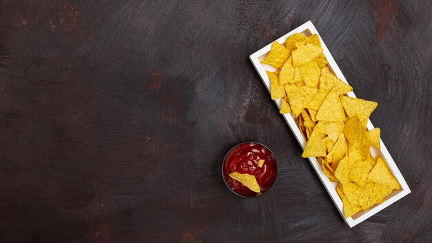 Nachos en plato blanco rectangular y salsa de tomate en un tazón pequeño