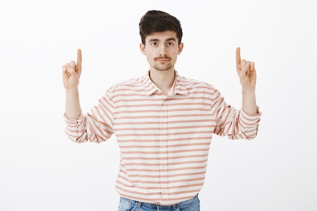 Nada interesante aqui. Retrato de indiferente chico guapo no impresionado con barba y bigote, levantando las manos, apuntando hacia arriba con expresión de calma disgustada, de pie