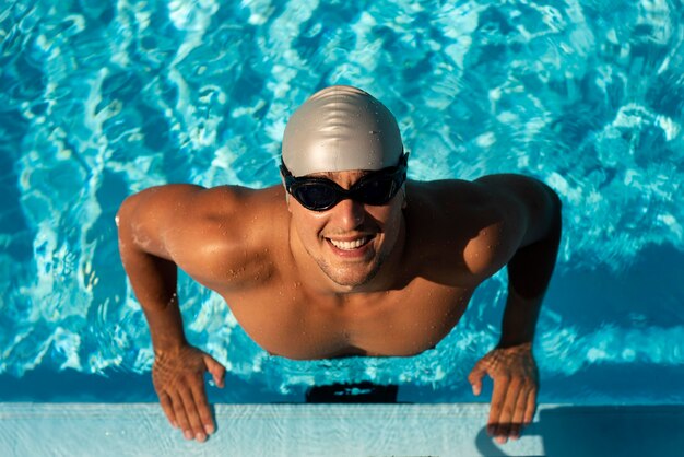 Nadador masculino sonriente posando con gafas y gorra en la piscina