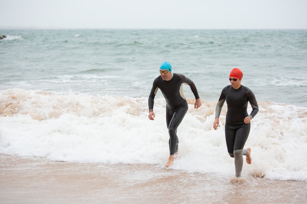 Foto gratuita nadadores en trajes de neopreno corriendo en las olas del mar