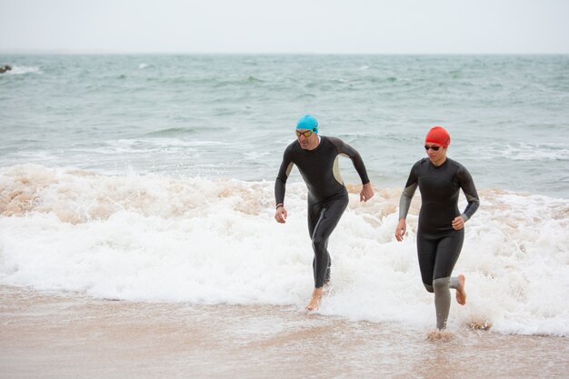 Nadadores en trajes de neopreno corriendo en las olas del mar