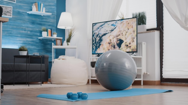 Nadie en la sala de estar con equipamiento deportivo en el piso. Lugar vacío con mancuernas, pelota tonificante stretch y esterilla de yoga para realizar ejercicio físico y practicar fitness, gimnasia y pilates.