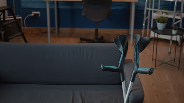 Nadie en la sala de estar con equipo de transporte y muletas en el sofá. Espacio vacío con objetos de movilidad para ayudar al paciente con discapacidad física, brindando ayuda para recuperarse del problema de caminar.