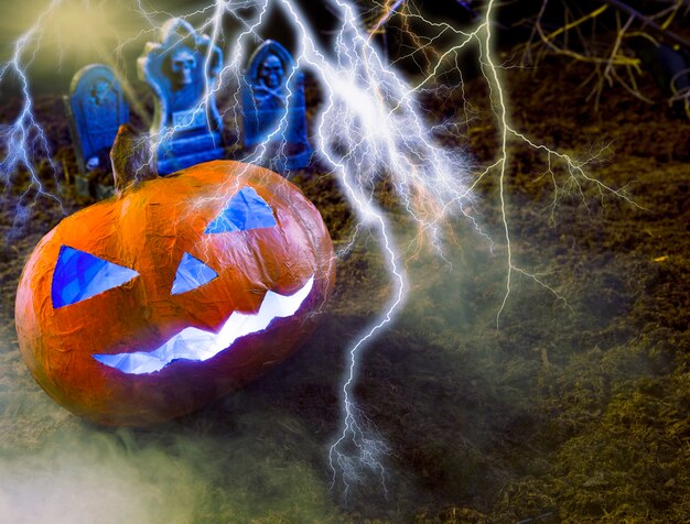 Naranja calabaza hecha a mano con cara tallada en estilo Halloween con relámpagos y lápidas detrás