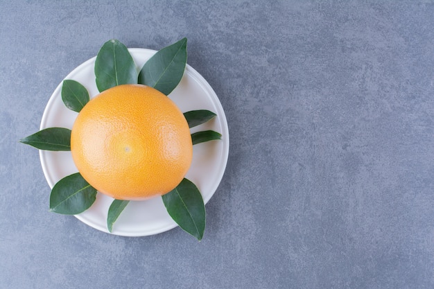 Naranja jugosa madura con hojas en placa sobre mesa de mármol.