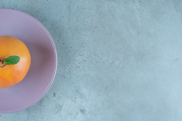 Naranja madura fresca en un plato, sobre el fondo de mármol.