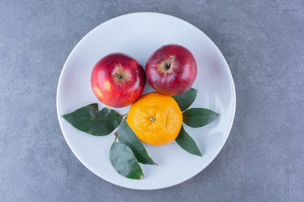 Naranja y manzanas con hojas en la placa sobre la superficie oscura