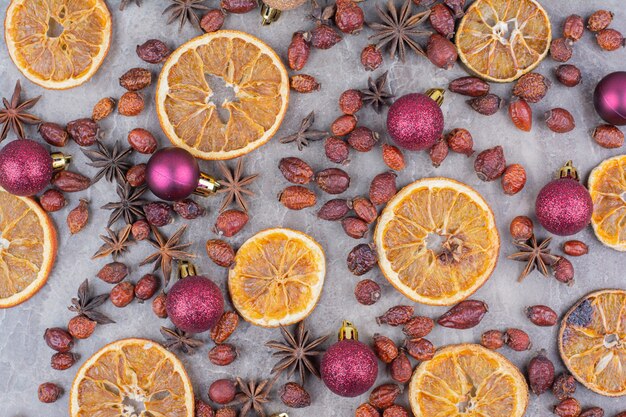 Naranja seca con bolas de Navidad y rosa mosqueta sobre la superficie de piedra.