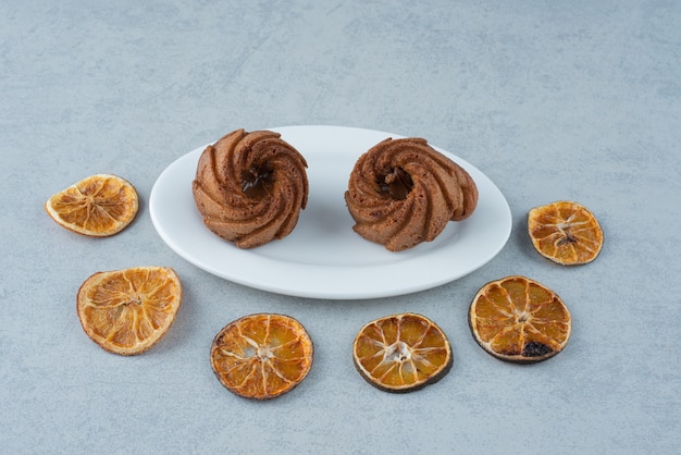 Naranja seca con dos deliciosos cupcakes sobre fondo blanco.