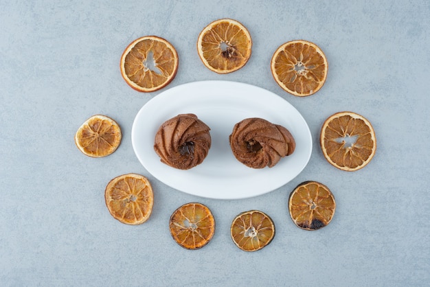 Naranja seca con dos deliciosos cupcakes sobre fondo blanco.