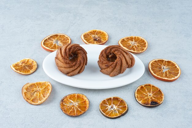 Naranja seca con dos deliciosos cupcakes sobre fondo blanco.