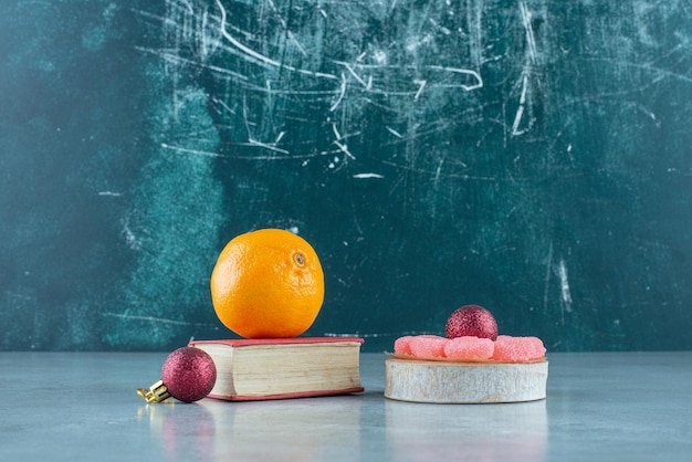 Naranja sobre libro, mermeladas sobre pieza de madera y dos bolas decorativas sobre mármol.