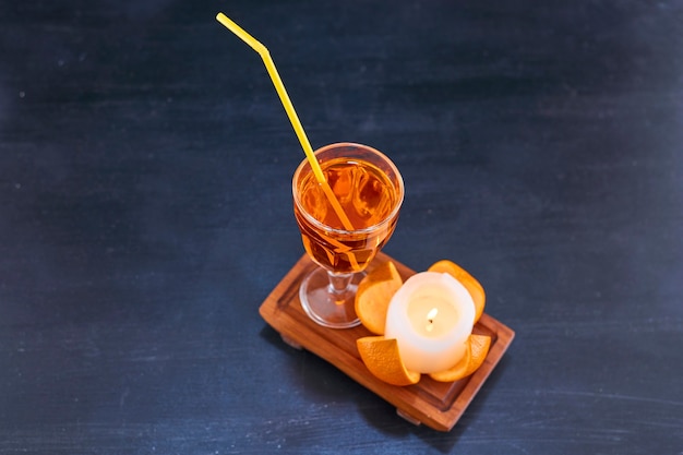 Naranja y un vaso de jugo con tubo amarillo en bandeja de madera, vista de ángulo