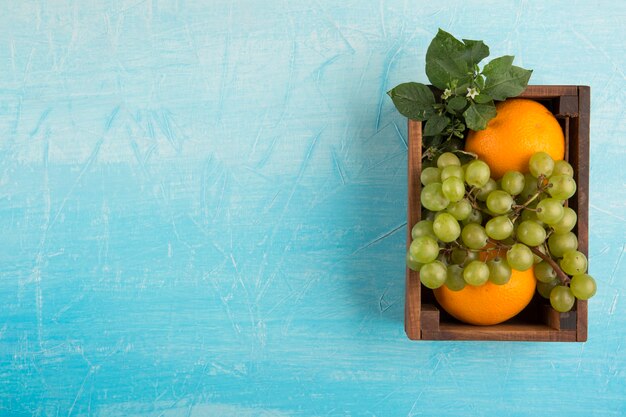 Naranjas amarillas y un racimo de uva en una caja de madera en el centro