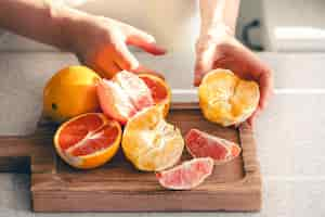 Foto gratuita naranjas descascaradas en manos femeninas y en una tabla de cortar de madera para el jugo