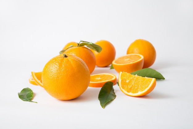 Naranjas enteras brillantes con hojas verdes y frutas cortadas