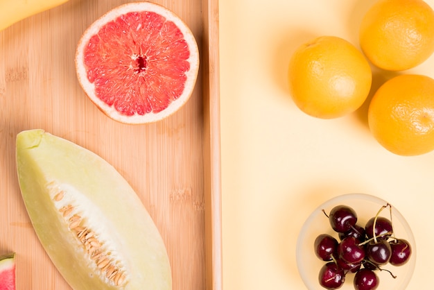 Foto gratuita naranjas enteras; cerezas rojas; pomelo a la mitad y melón en escritorio de madera