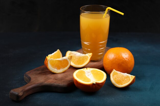 Naranjas enteras y en rodajas con un vaso de jugo.