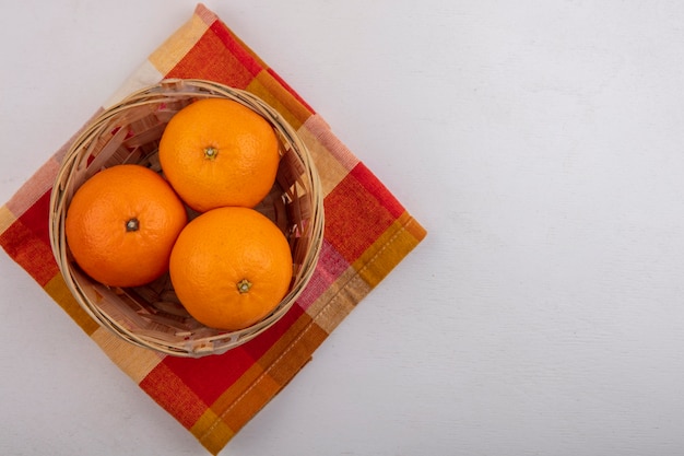 Foto gratuita naranjas del espacio de la copia de la vista superior en la cesta en la toalla a cuadros sobre fondo blanco