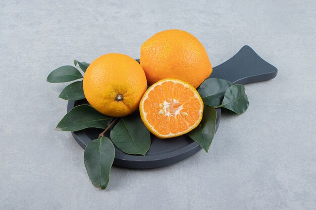 Naranjas frescas con hojas sobre tabla de cortar negra