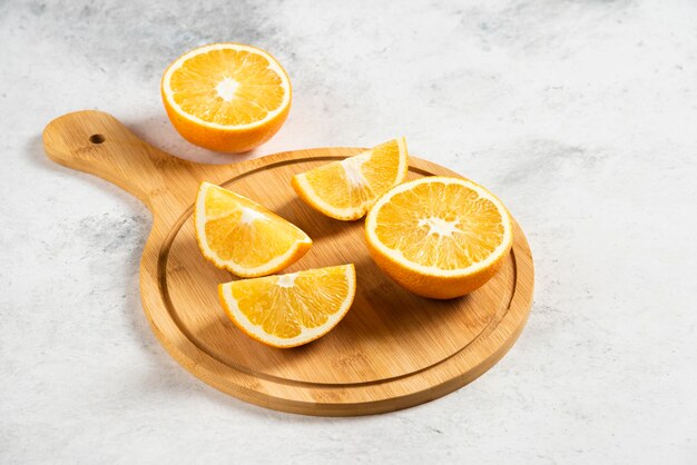 Naranjas frescas en rodajas con escariador de madera sobre mármol.