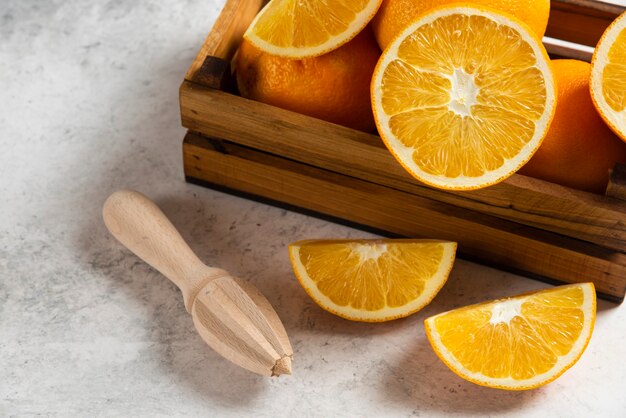 Naranjas frescas en rodajas con escariador de madera sobre mármol.