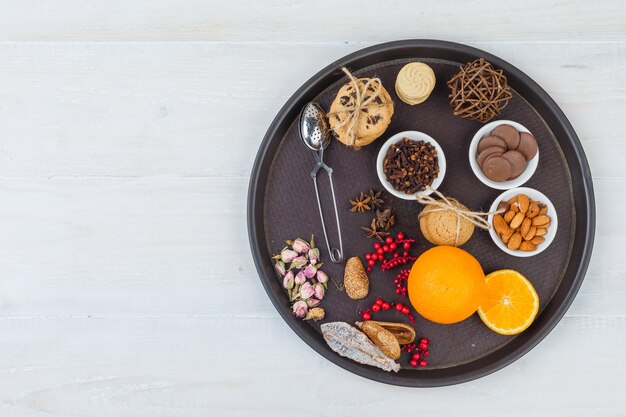 Naranjas y galletas en bandeja con colador de té, hierbas y especias