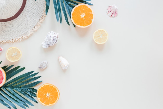 Naranjas con hojas de palmera, conchas y sombrero de paja.