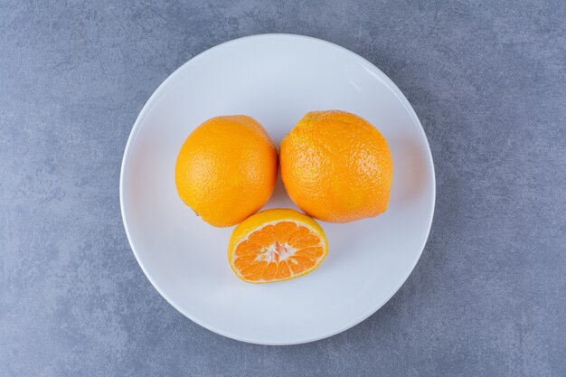 Naranjas jugosas en un plato, sobre la superficie oscura