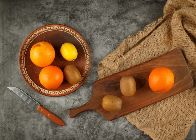 Naranjas y kiwies en un tazón y en la tabla de cortar.