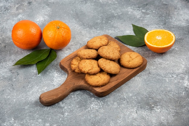 Naranjas orgánicas frescas enteras o cortadas y galletas caseras sobre tabla de madera.