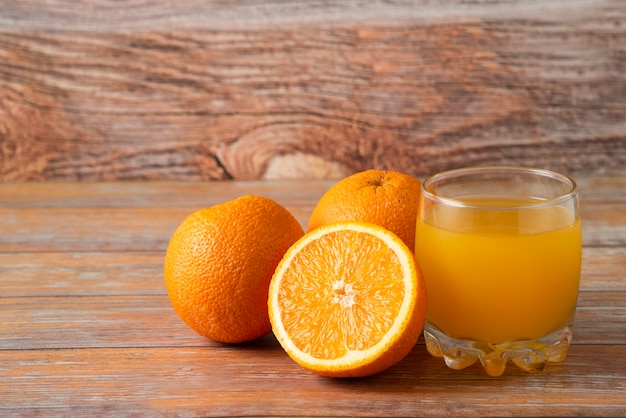Naranjas y un vaso de jugo aislado en madera