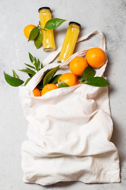 Naranjas de vista superior en bolso de mano con botellas de jugo