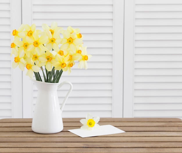 Narciso cabezas de flores en la mesa de madera marrón tarjeta de invitación blanca tempate y persianas blancas