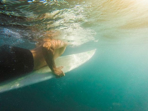 Natación del hombre joven en la tabla hawaiana en agua azul