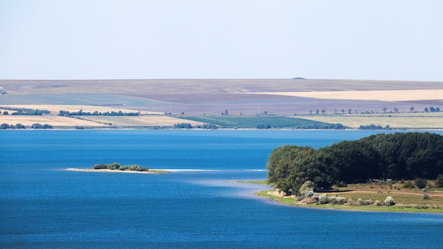 Naturaleza de Moldavia, lago con isla pequeña, prado con frondosos árboles a la derecha, amplios campos visibles en la distancia