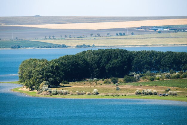 Naturaleza de Moldavia, prado con camino de pueblo, frondosos árboles y gente descansando, lago, campos y edificios raros visibles en la distancia