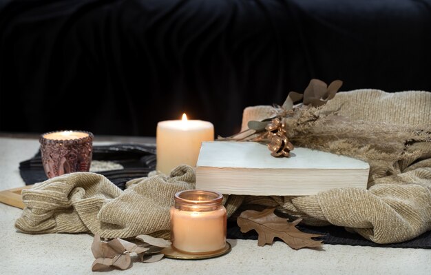 Naturaleza muerta sobre la mesa un libro, una vela, té en el espacio de un sofá oscuro. Concepto de comodidad de otoño.