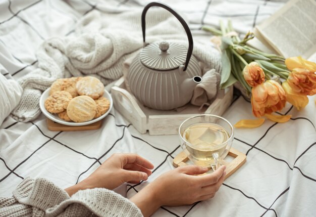 Naturaleza muerta con una taza de té, una tetera, un ramo de tulipanes y galletas en la cama. Concepto de fin de semana y mañana de primavera.