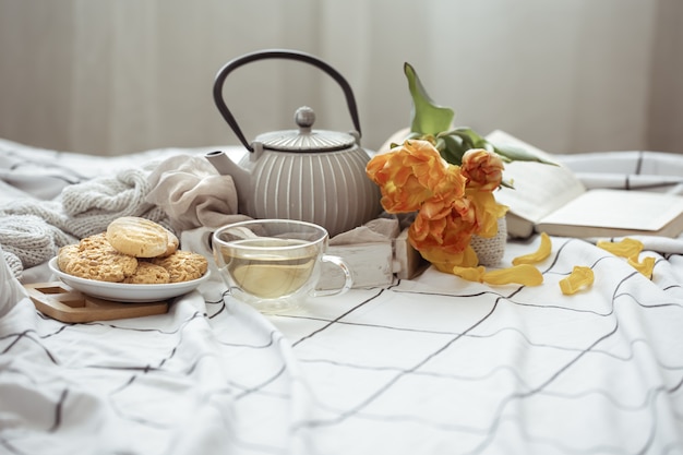 Naturaleza muerta con una taza de té, una tetera, un ramo de tulipanes y galletas en la cama. Concepto de fin de semana y mañana de primavera.