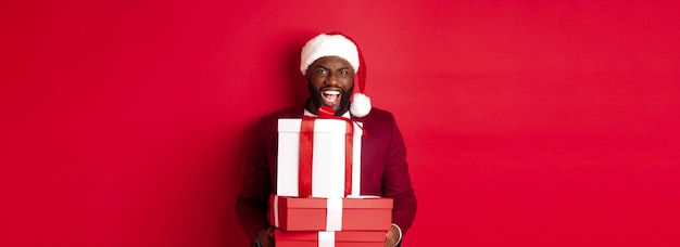 Foto gratuita navidad año nuevo y concepto de compras feliz hombre negro con sombrero de santa y blazer con regalo de navidad