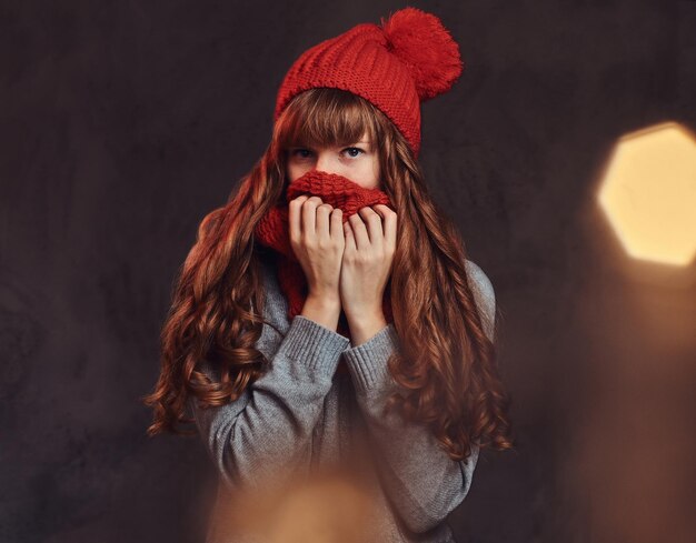 Navidad, San Valentín, Año Nuevo. Retrato de una hermosa pelirroja con un suéter cálido, se cubre la cara con una bufanda.