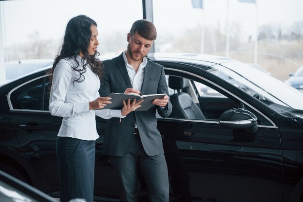 Necesito firmar ese documento. Clienta y empresario barbudo con estilo moderno en el salón del automóvil