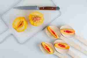 Foto gratuita nectarinas con cuchillo en cucharas de madera sobre mesa blanca y tabla de cortar, endecha plana.