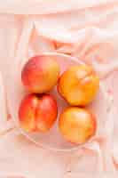Foto gratuita nectarinas frescas en un plato en la superficie textil rosa, vista de ángulo alto.