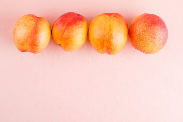 Foto gratuita nectarinas frescas sobre una superficie rosa. aplanada