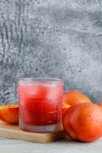 Nectarinas con jugo, tabla de cortar en la pared sucia, vista lateral.