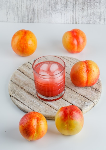 Nectarinas con jugo, tabla de cortar, vista de ángulo alto en la pared blanca y sucia