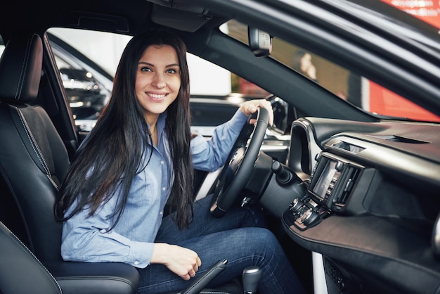 Negocio automotriz, venta de automóviles, consumismo y concepto de personas: mujer feliz que toma el automóvil del concesionario en el salón del automóvil