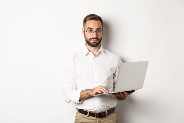 Foto gratuita negocio. joven empresario guapo trabajando en equipo portátil, haciendo trabajo en equipo, de pie